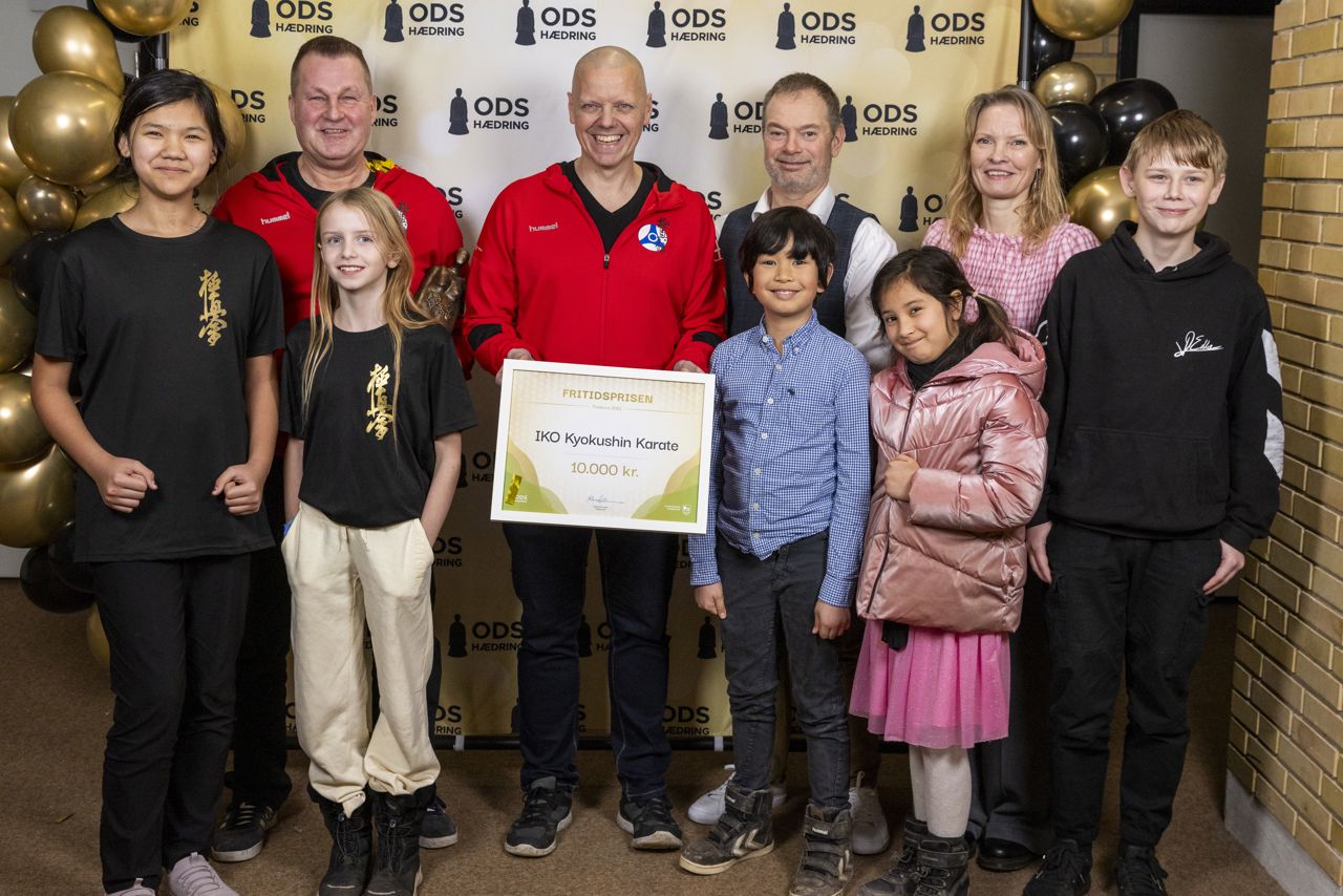 Børn og voksne fra karateklubben tager gruppebillede med pris bag pressevæg